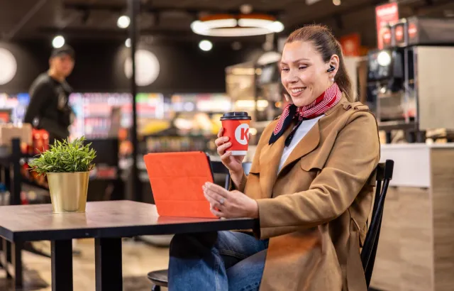 Woman on her tablet with a hot drink in Circle K