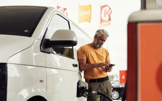 Man looking relaxed while fueling his car at a Circle K station, looking at his phone
