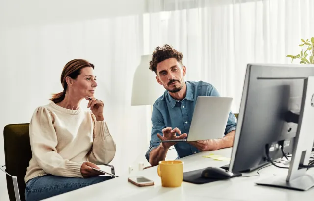 Person showing woman how to use customer portal on their laptop, at a desk