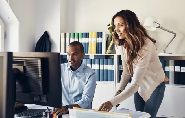 Man and woman in office looking at computer monitor with interest together